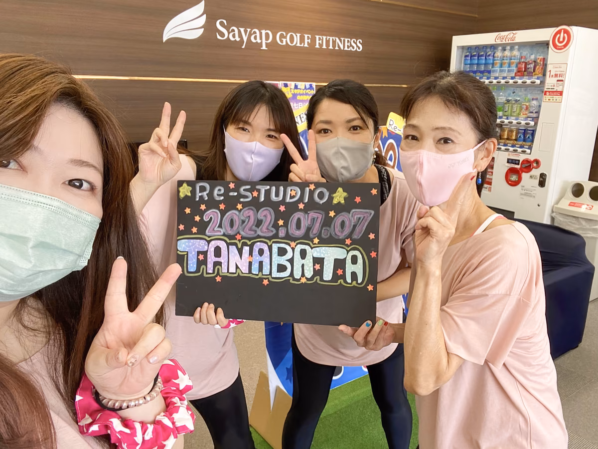 マスクを着けた4人の女性が、手でピースを作りながら「2022 07 07 TANABATA」と書かれた黒いボードを持っている。