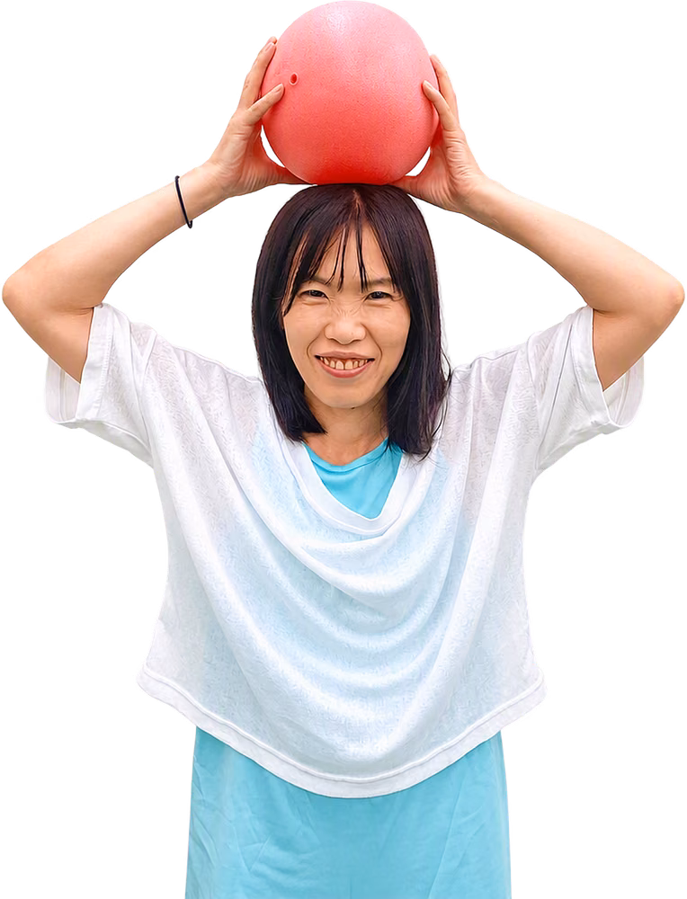 赤いボールを両手で頭の上にのせて笑う女性。