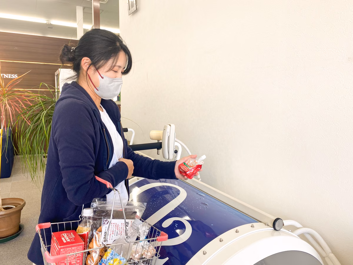 マスクを着けた女性が買い物かごを持ち、レジで商品を手に取っている様子。