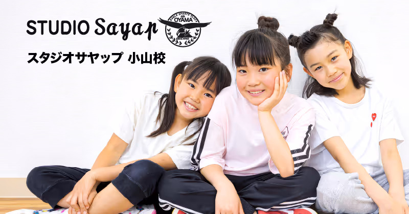 白い背景の前で座っている三人の笑顔の子供たち、左から黒いパンツと白いシャツ、ピンクのシャツと黒いパンツ、白いシャツとグレーのパンツを着ている。