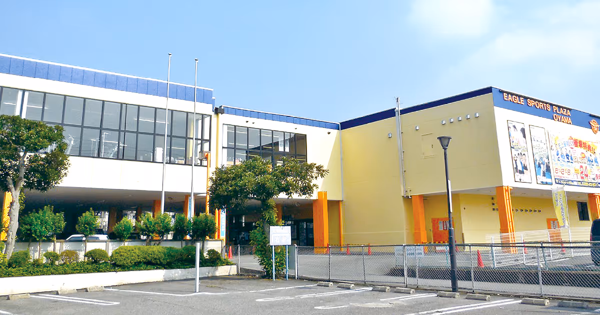 Eagle Sports Plaza Oyamaの建物外観、青空の下に黄色と白の壁とオレンジの柱が見える。