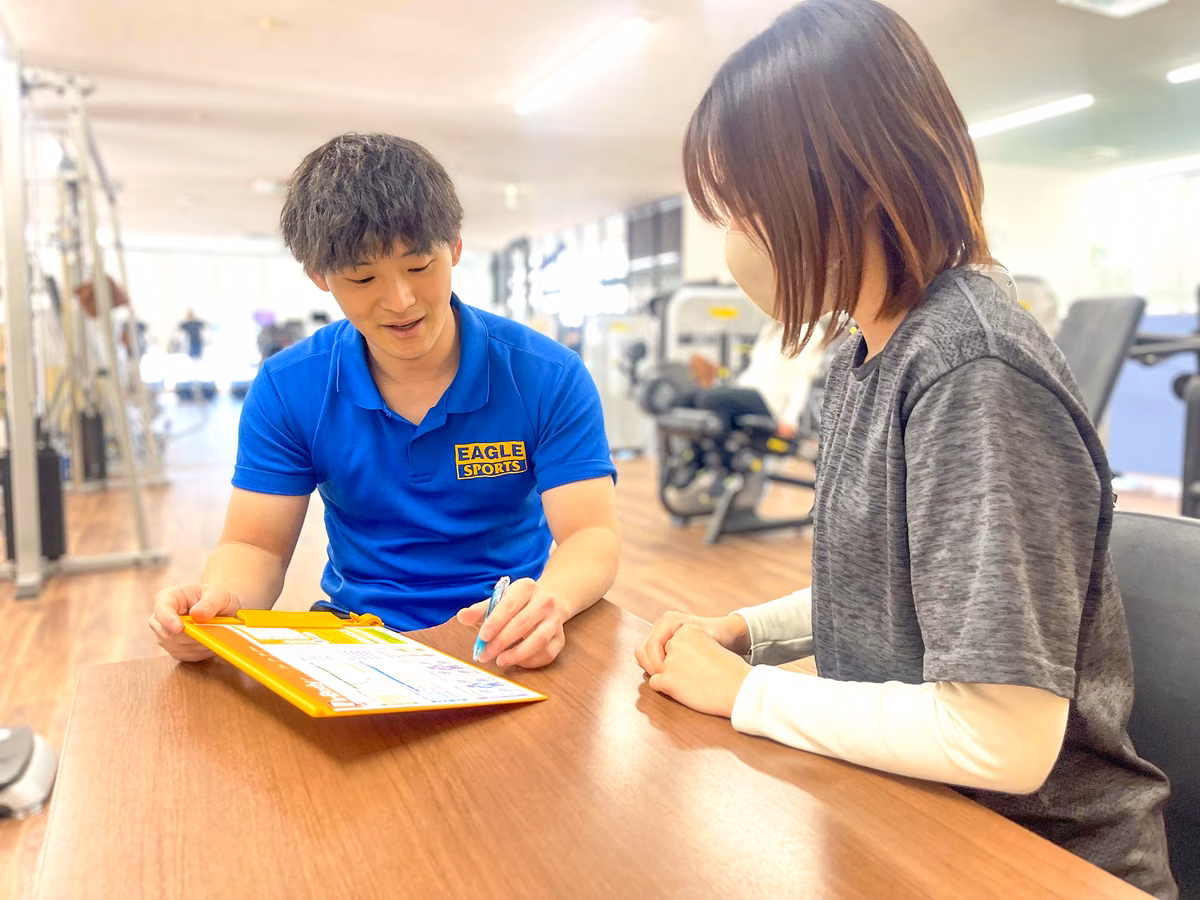 トレーナーが用紙に書き込みながら、会員と向かい合って話している様子。