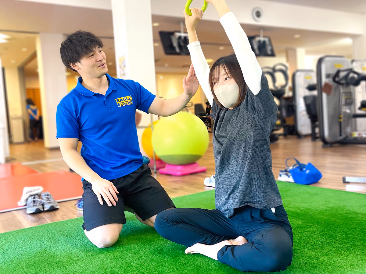 人工芝の上で両腕を上げる会員の動きを、トレーナーが横で確認している様子。