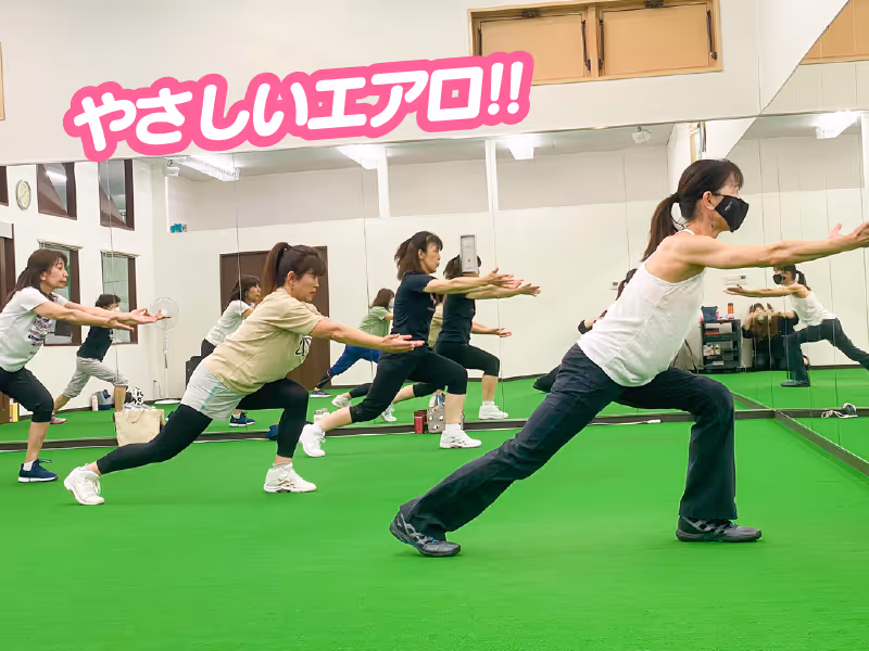 マスクを着用した女性たちが鏡の前で足を広げて腕を前に伸ばし、ストレッチ運動をしているジムの様子。