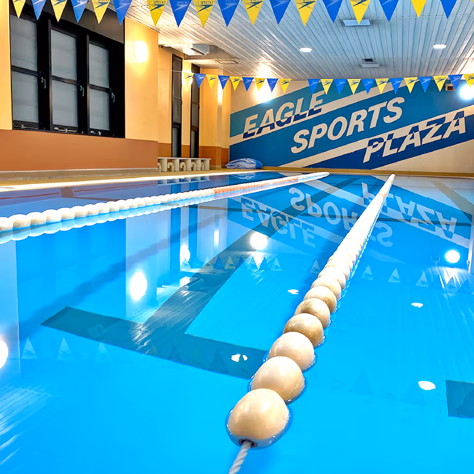 室内プールに浮かぶレーンロープと壁に「EAGLE SPORTS PLAZA」と書かれた青い看板。