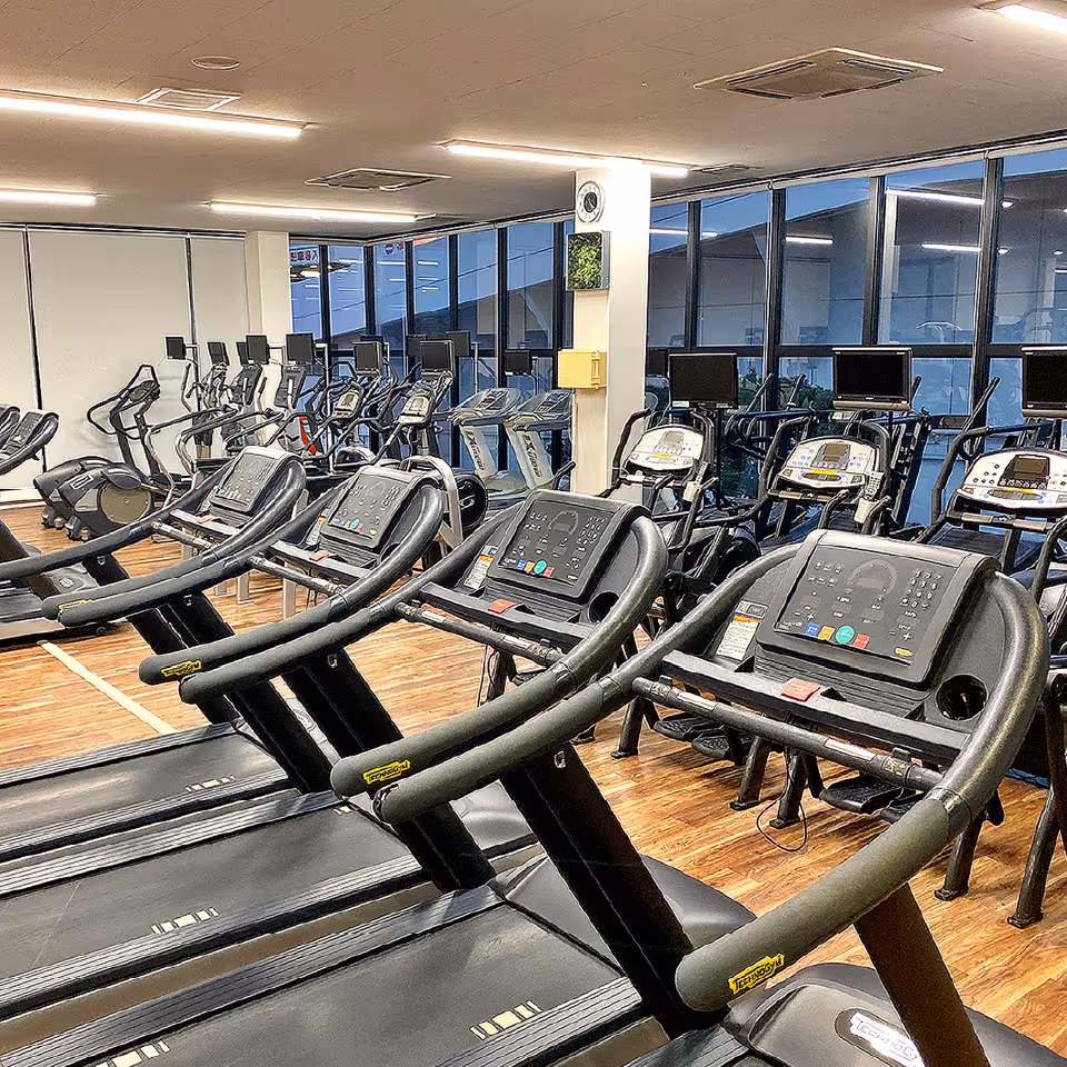 ジムの木目フロアに並ぶ複数のトレッドミルとフィットネスマシン。